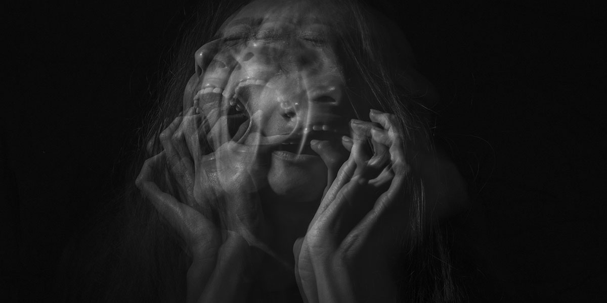 Schwarz weißes Porträt, bei dem Gesicht und Hände einer Person übereinander verschwimmen. Angststörung unsichtbar