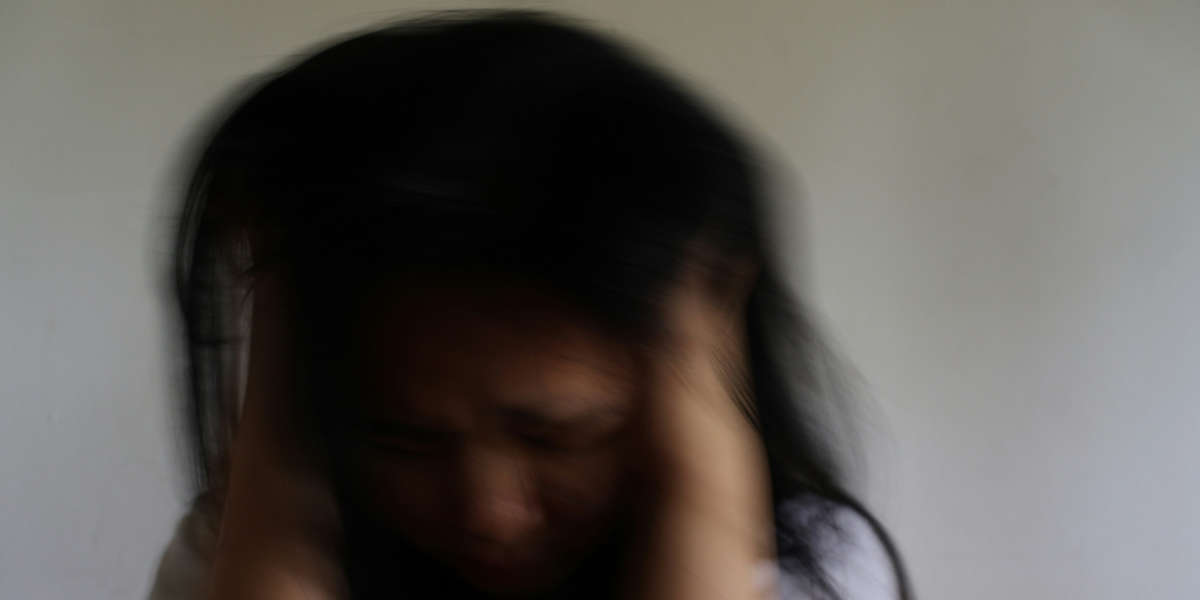 Eine unscharfe Aufnahme einer Person, die sich mit beiden Händen an den Kopf fasst.